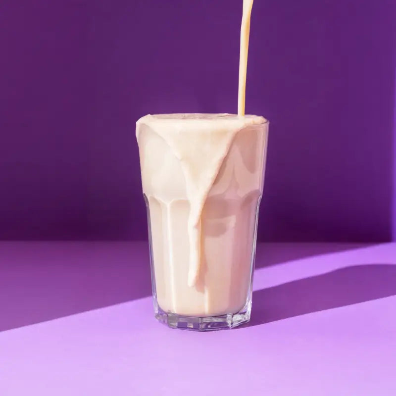 Glass of creamy vanilla flavored protein powder on a table with a potted plant in the background
