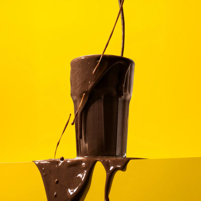 Black protein powder bag with a purple label next to a glass of chocolate protein powder on a light background